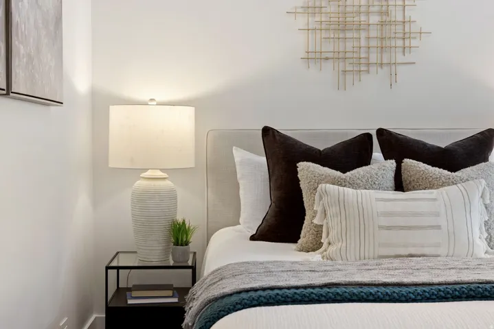 Upholstered headboard with an art installation, accompanied by a glass-top nightstand and a textured ceramic table lamp