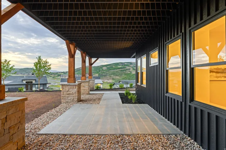 Covered outdoor patio featuring stone column bases, exposed wood beams, and a concrete walkway