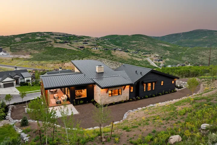 Modern architectural residence featuring a dark metal roof, stone and dark siding exterior, covered outdoor patio with wood-finish decking, and expansive windows