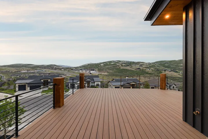 Expansive outdoor deck featuring wood-finish decking, black metal railing with wood posts, and an overhead soffit with recessed lighting