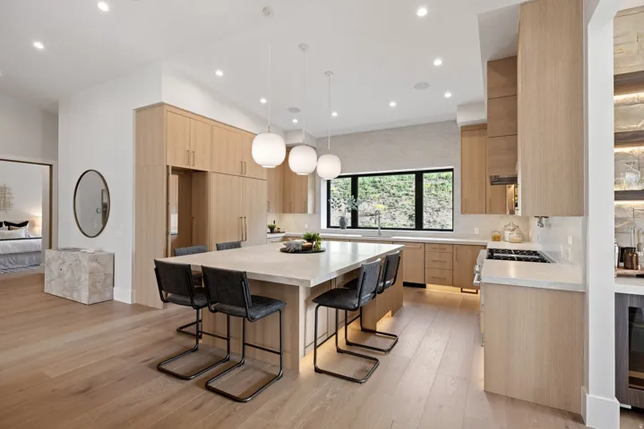 Gourmet kitchen featuring a substantial island with seating, integrated appliances, natural wood-finish cabinetry, light-toned countertops, and a modern window with dark trim