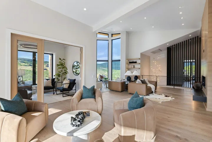 Spacious living area featuring high ceilings, wood-finish flooring, a wall of large windows, and an integrated fireplace with a dark stone hearth