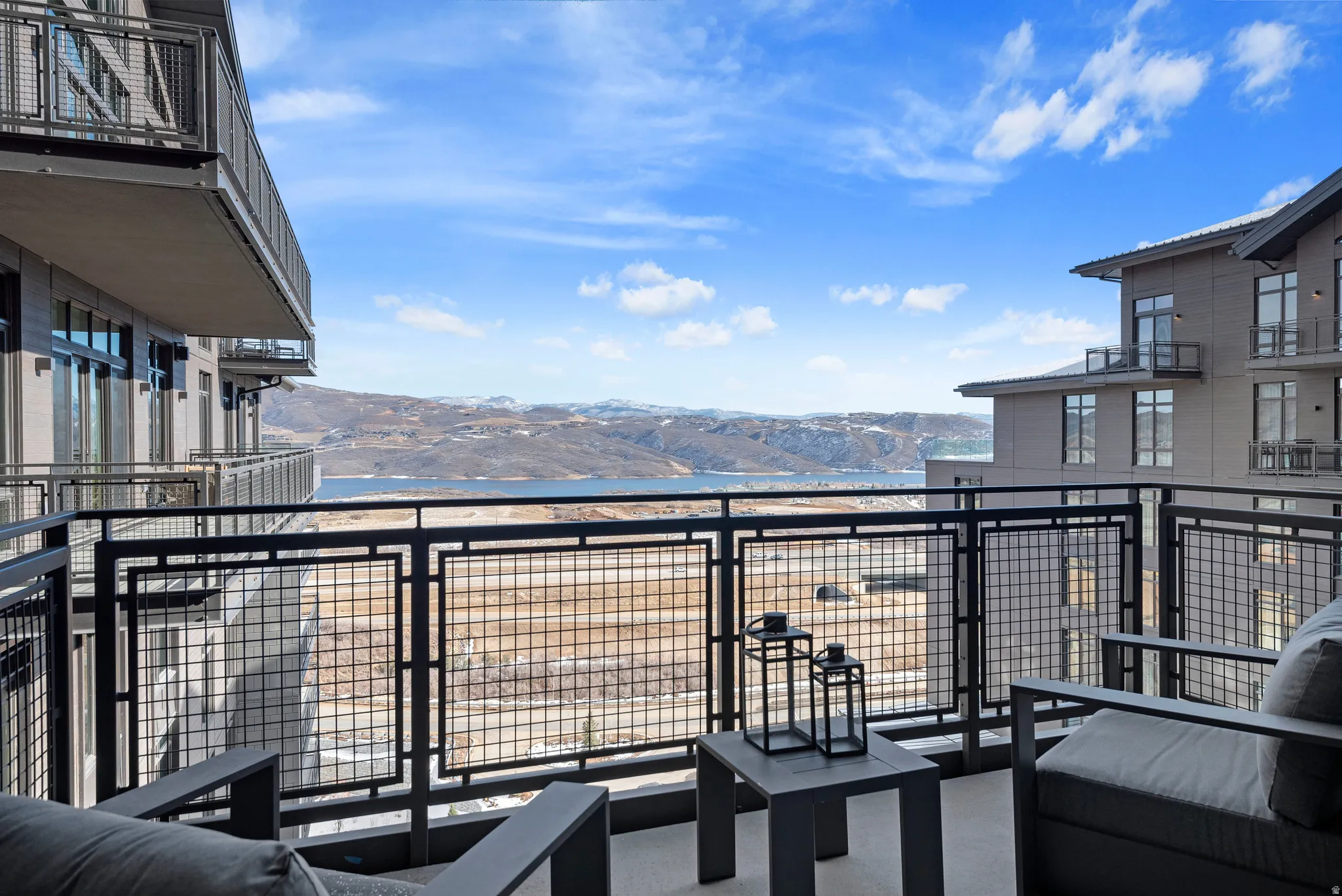 Private balcony with metal railing, featuring concrete flooring and sweeping mountain and water scenery