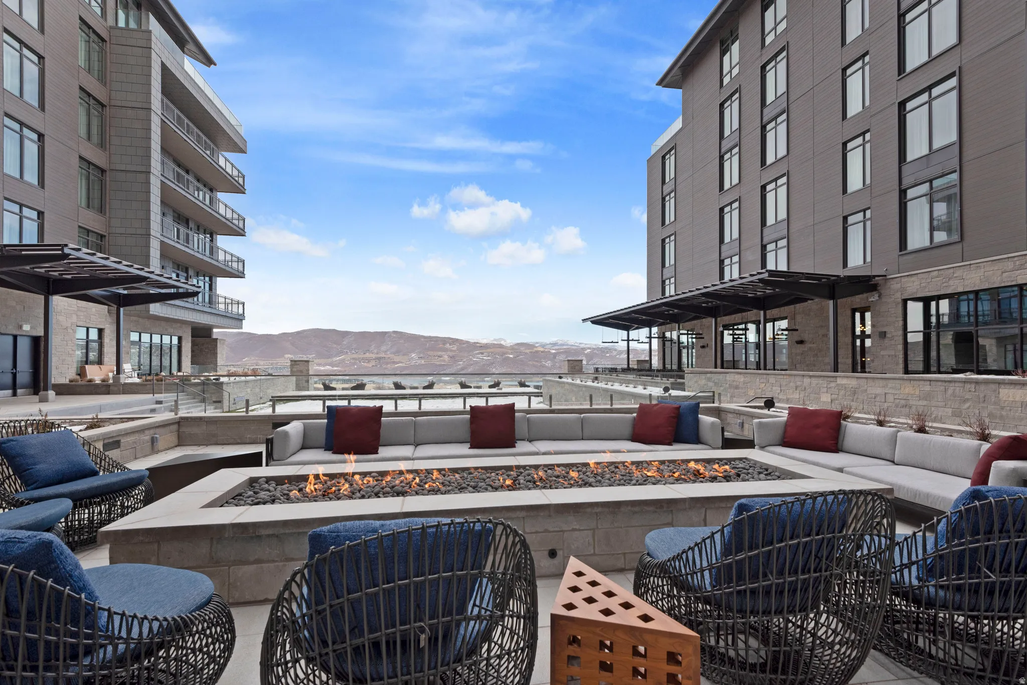 Outdoor patio featuring a rectangular fire pit with stone surround, integrated bench seating, and open-weave accent chairs