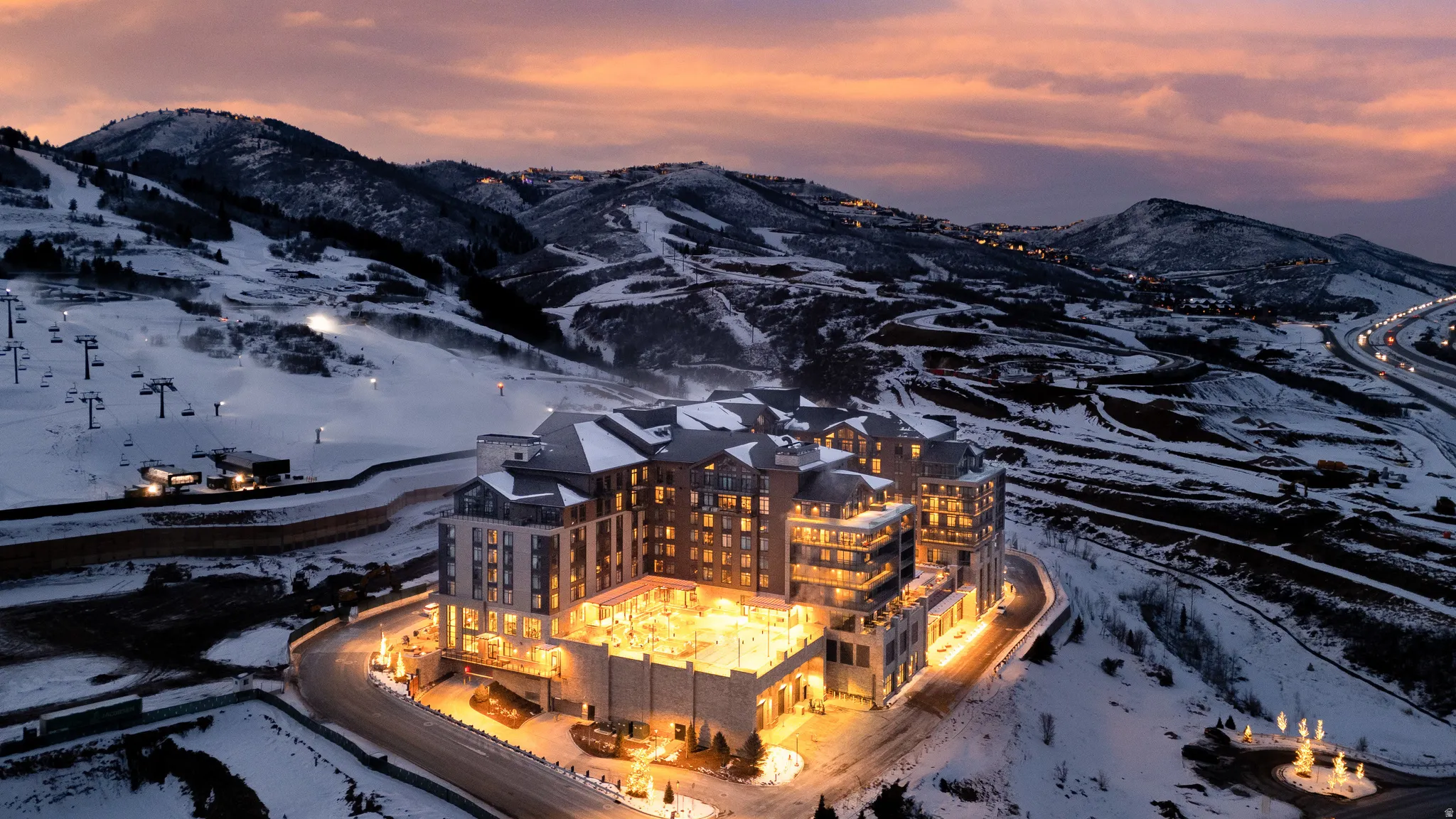 Expansive resort-style development featuring multiple buildings with illuminated exteriors, set against a snow-covered mountain backdrop