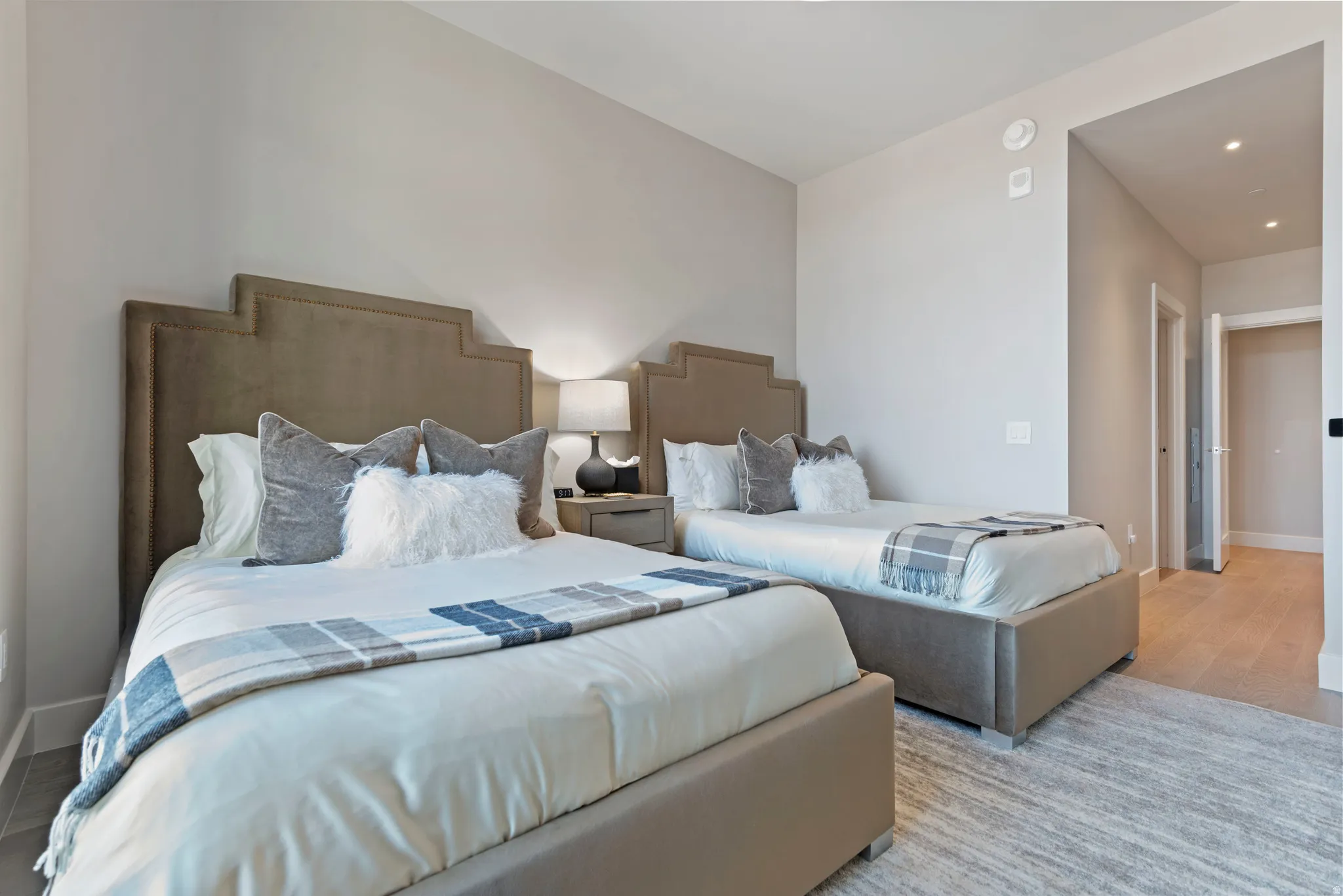 Spacious room featuring light-toned walls, recessed lighting, and light wood-finish flooring extending into the hallway
