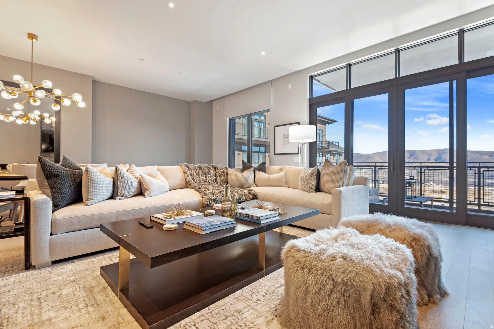 Living area featuring expansive floor-to-ceiling windows, light wood-finish flooring, recessed lighting, a contemporary chandelier, and a large balcony with a metal railing