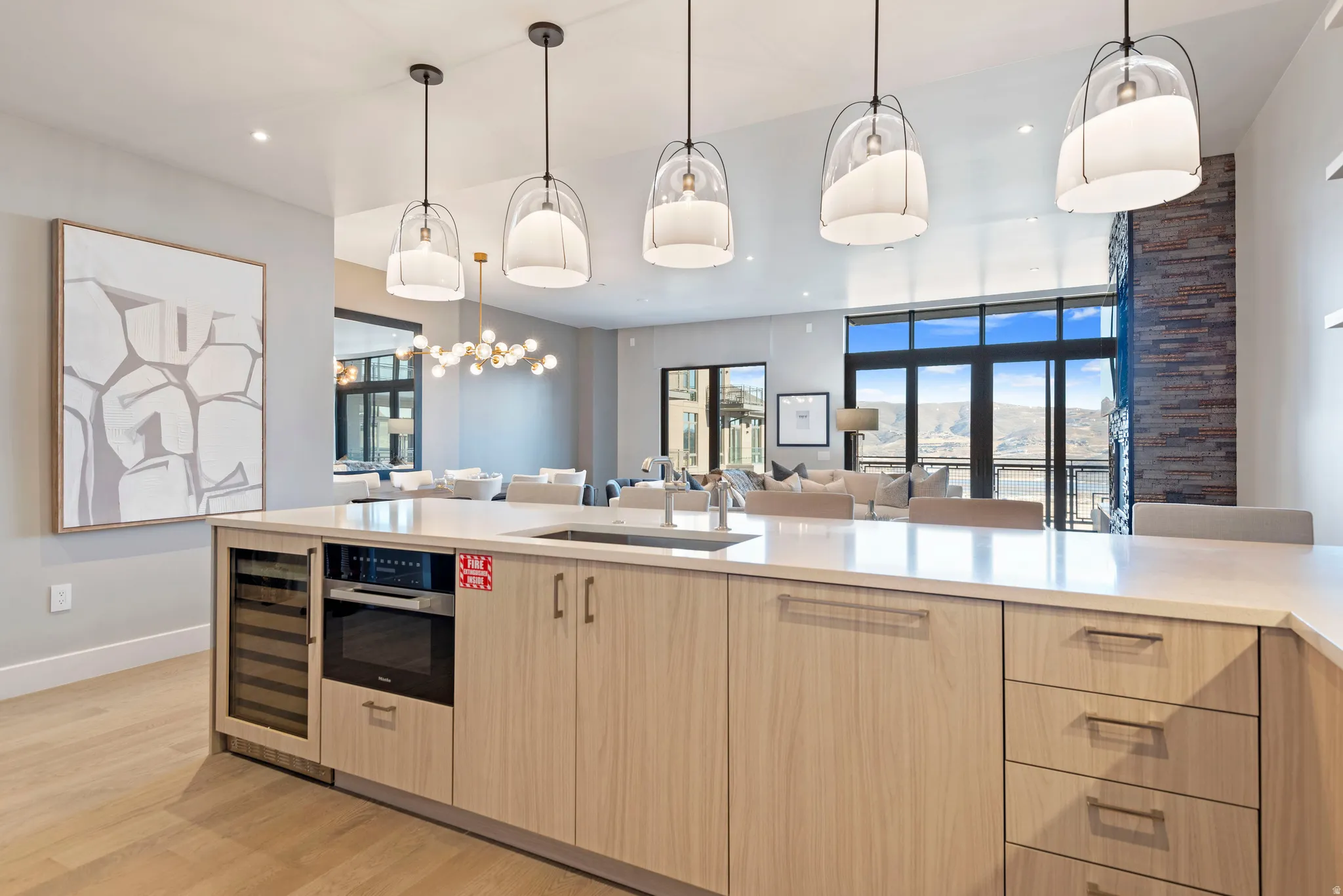 Spacious kitchen island featuring light wood-finish cabinetry, a built-in wine cooler, an integrated oven, and a sink with a gooseneck faucet