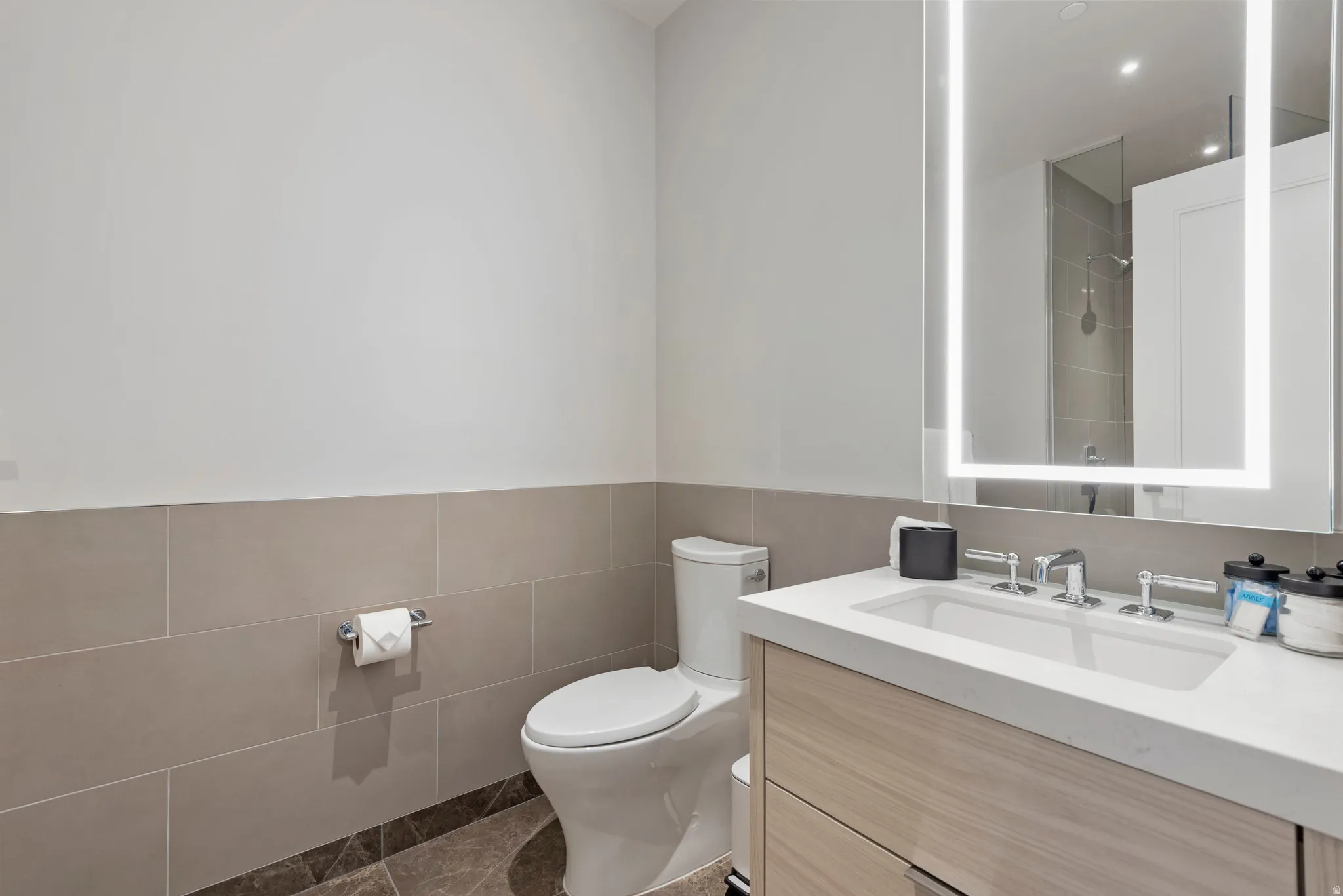 Bathroom featuring a wood-finish vanity with an integrated sink, polished chrome fixtures, and an illuminated mirror