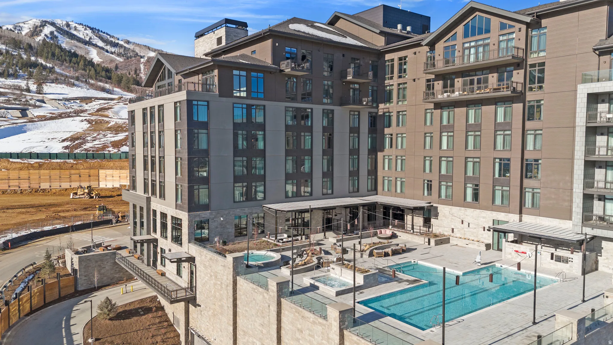 Contemporary multi-story building featuring extensive window-lines, private balconies, an outdoor swimming pool, and multiple hot tubs