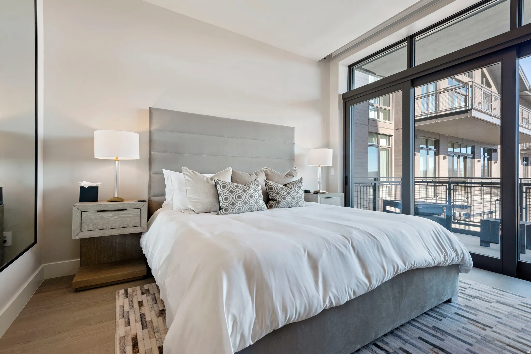 Spacious sleeping area featuring a full-height upholstered headboard, wood-finish flooring, and a large sliding glass door with transom windows