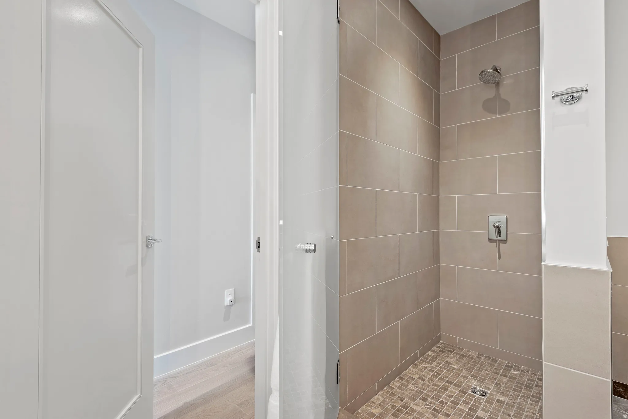 Walk-in shower featuring large format wall tiling, a rainfall showerhead, and pebble-style floor tiling