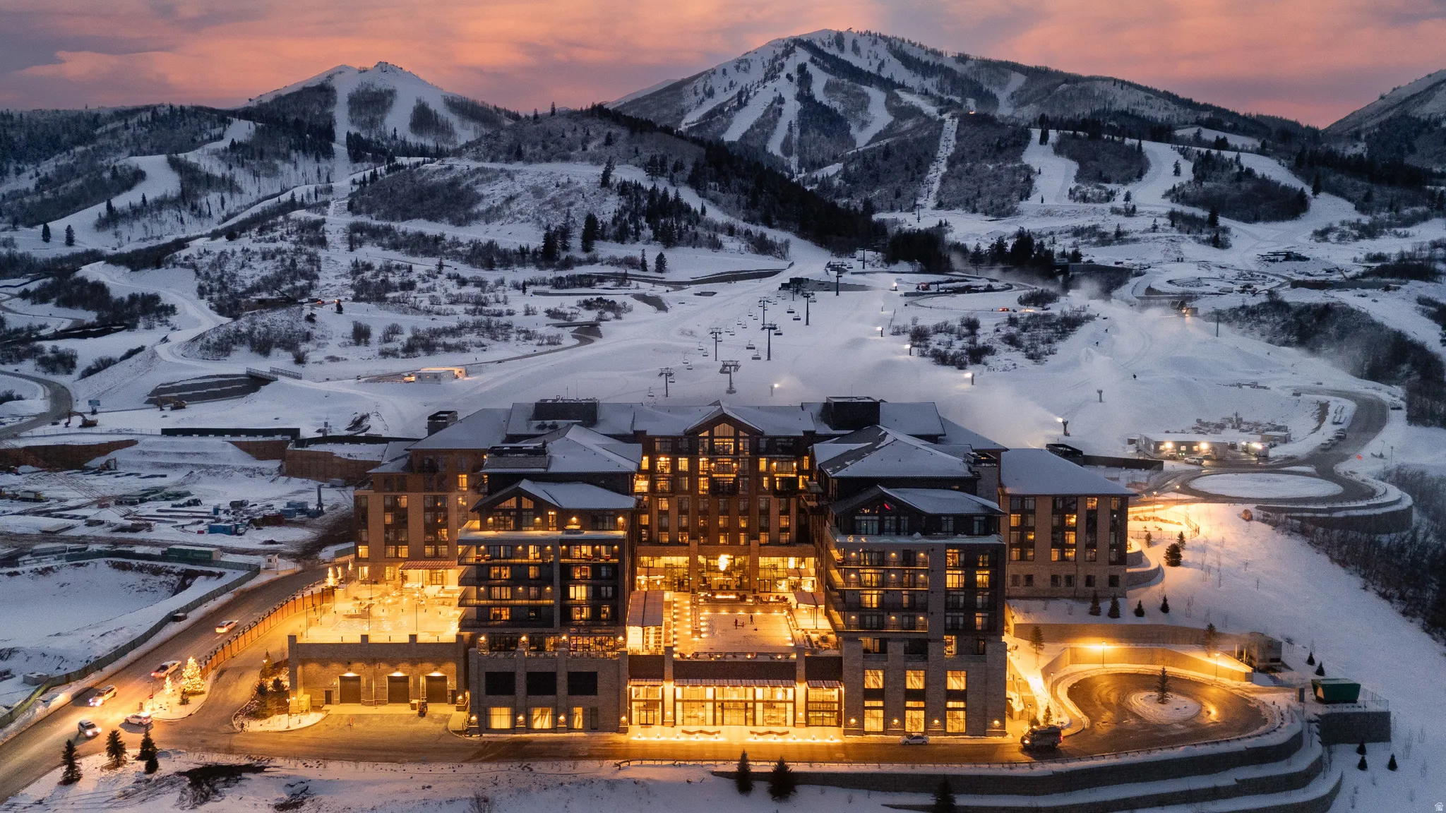 Large-scale property with multiple stories and extensive exterior lighting, situated within a snow-covered mountain landscape