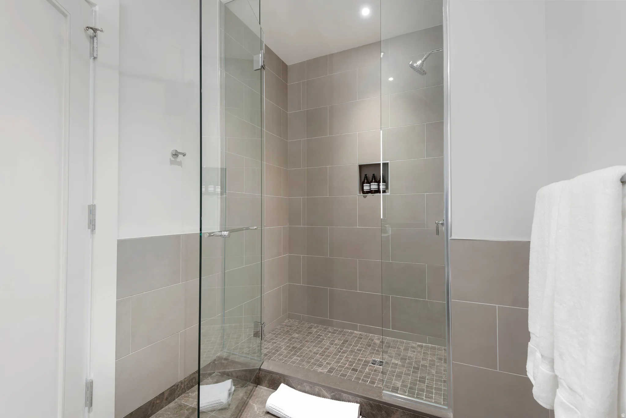 Glass-enclosed shower featuring a rainfall showerhead, tile-in niche, and textured pebble flooring