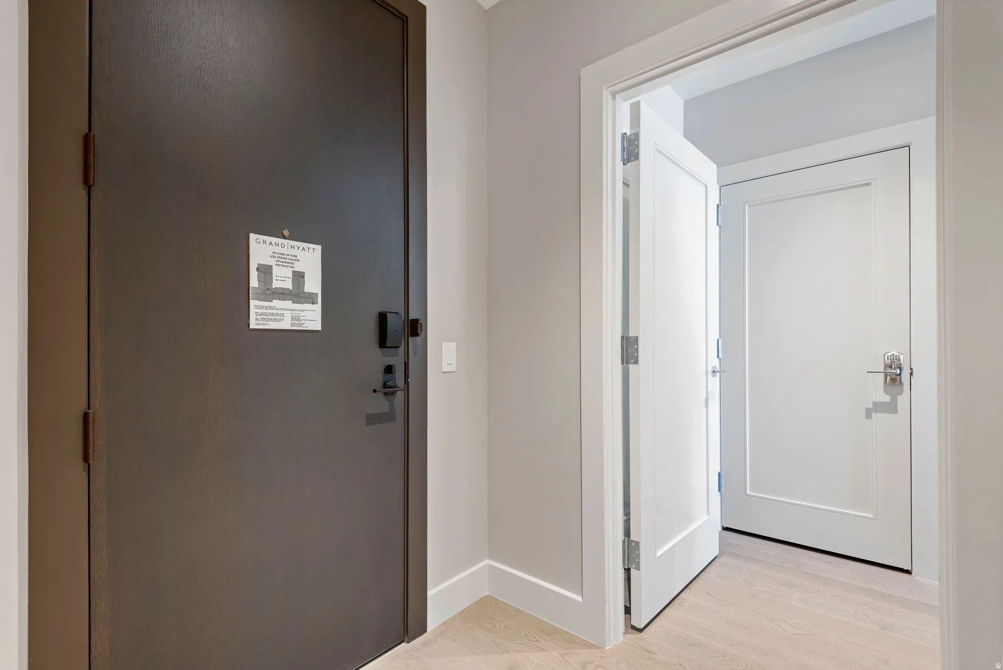 Entryway featuring a dark paneled door with digital lock, light wood-finish flooring, and light gray wall paint