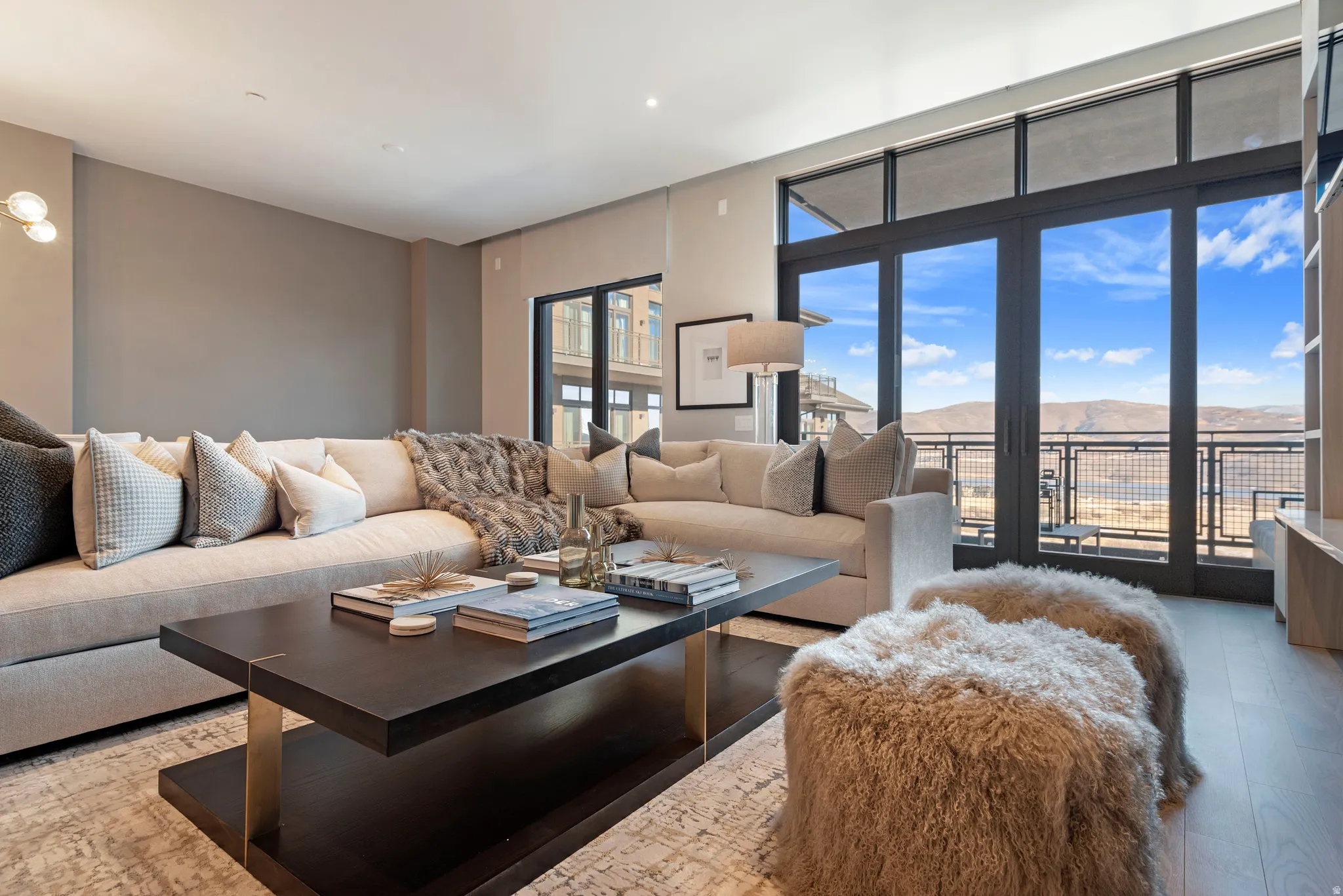 Spacious living area featuring expansive glass doors, wood-finish flooring, recessed lighting, a modern accent wall light fixture, and a built-in shelving unit