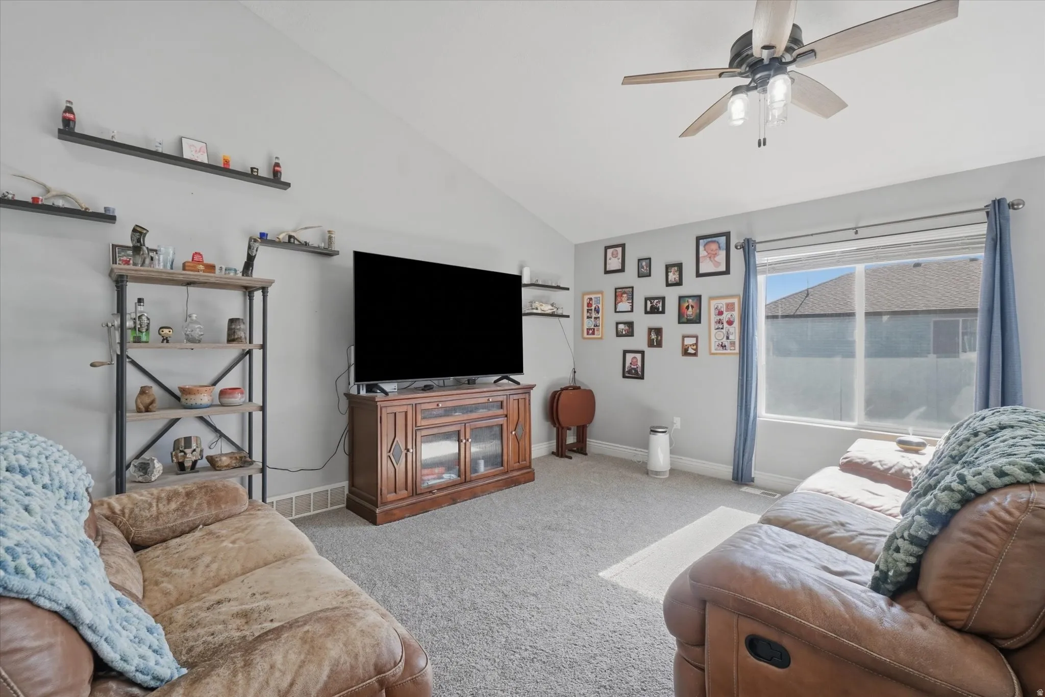 Vaulted ceilings enhance this living space featuring a ceiling fan, carpet flooring, and a large window