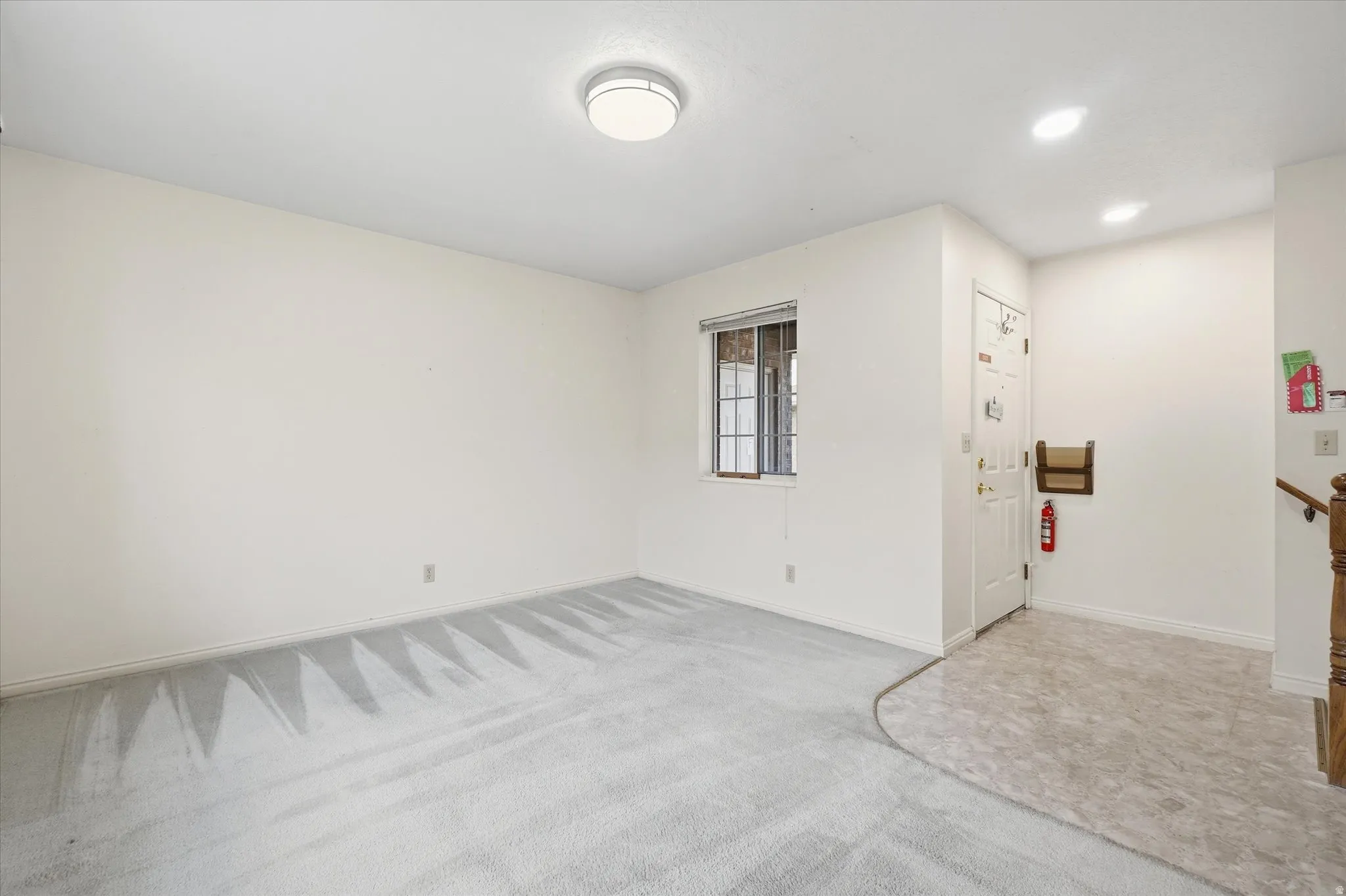 Expansive room featuring light-colored carpeting, a window with gridded panes, and a white entry door