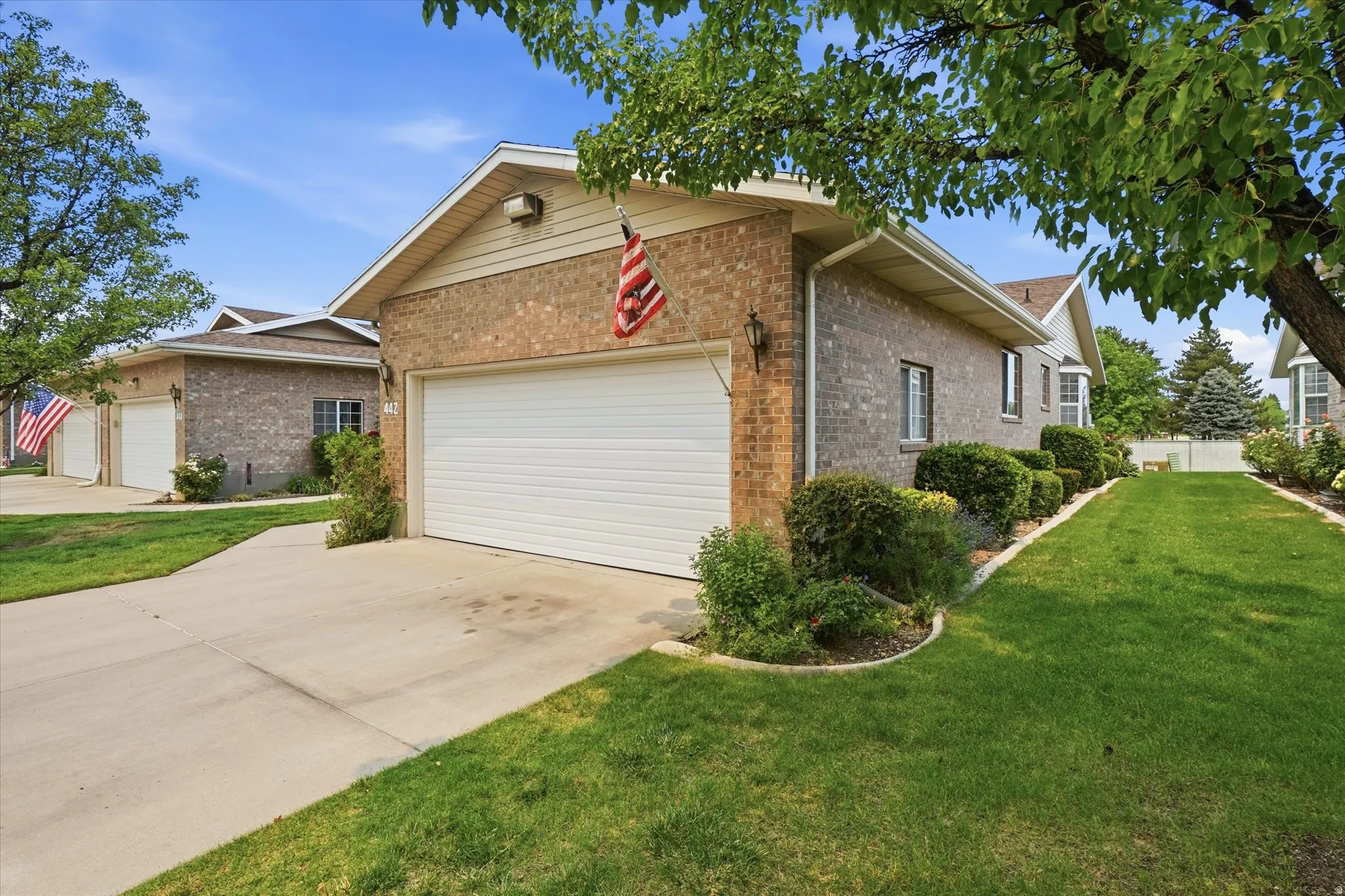Brick exterior with an attached garage, concrete driveway, and side yard featuring mature landscaping