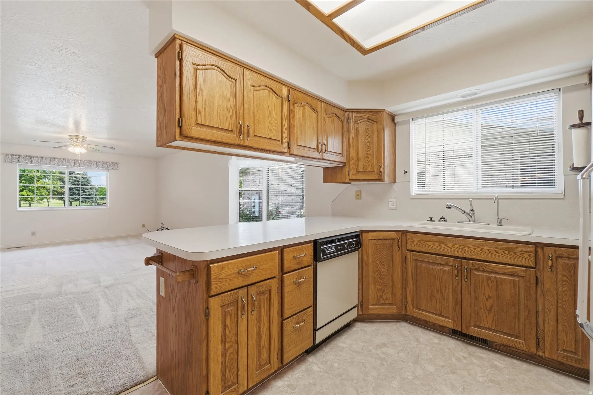 Kitchen featuring wood cabinetry, white countertops, a built-in dishwasher, and a double basin sink with a window above