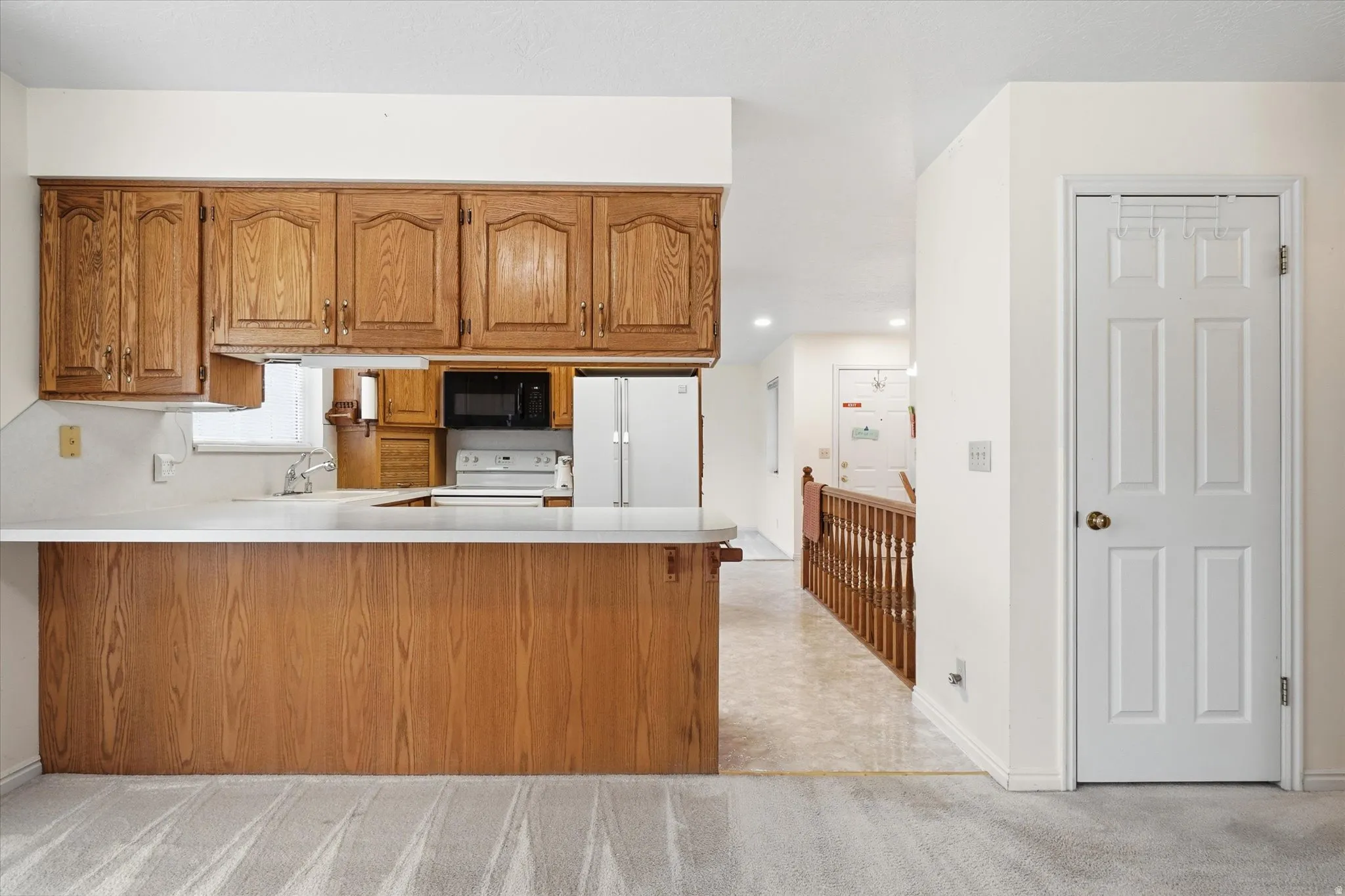 Kitchen featuring wood cabinetry, white countertops, built-in microwave, white refrigerator, and a breakfast bar peninsula
