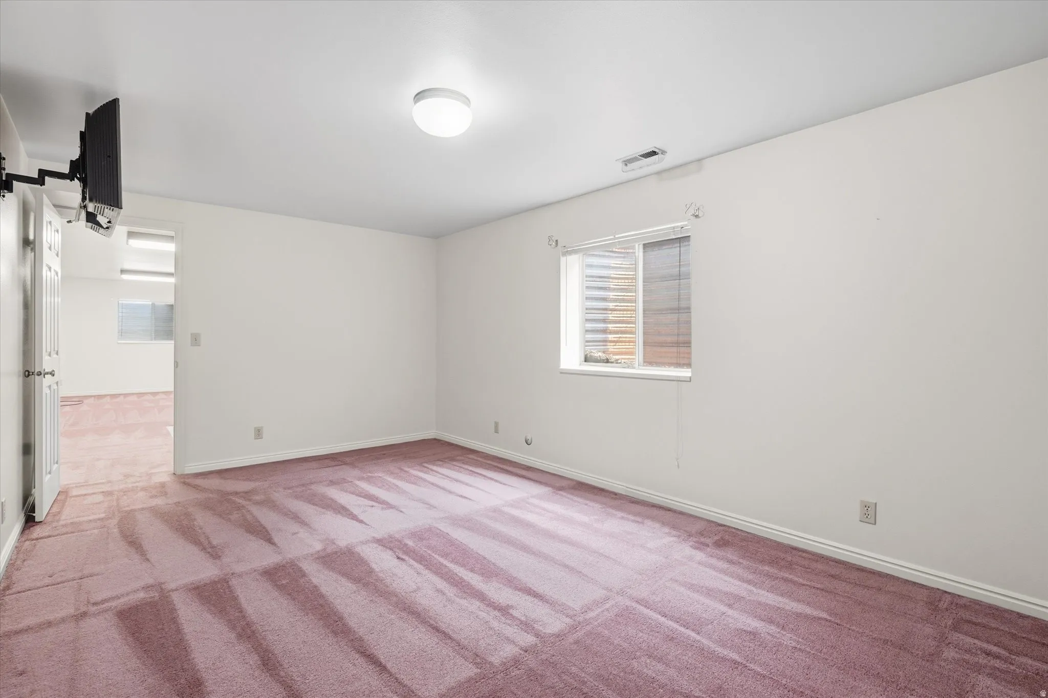 Spacious interior room featuring wall-to-wall carpeting, a flush-mount ceiling light fixture, and a window with blinds