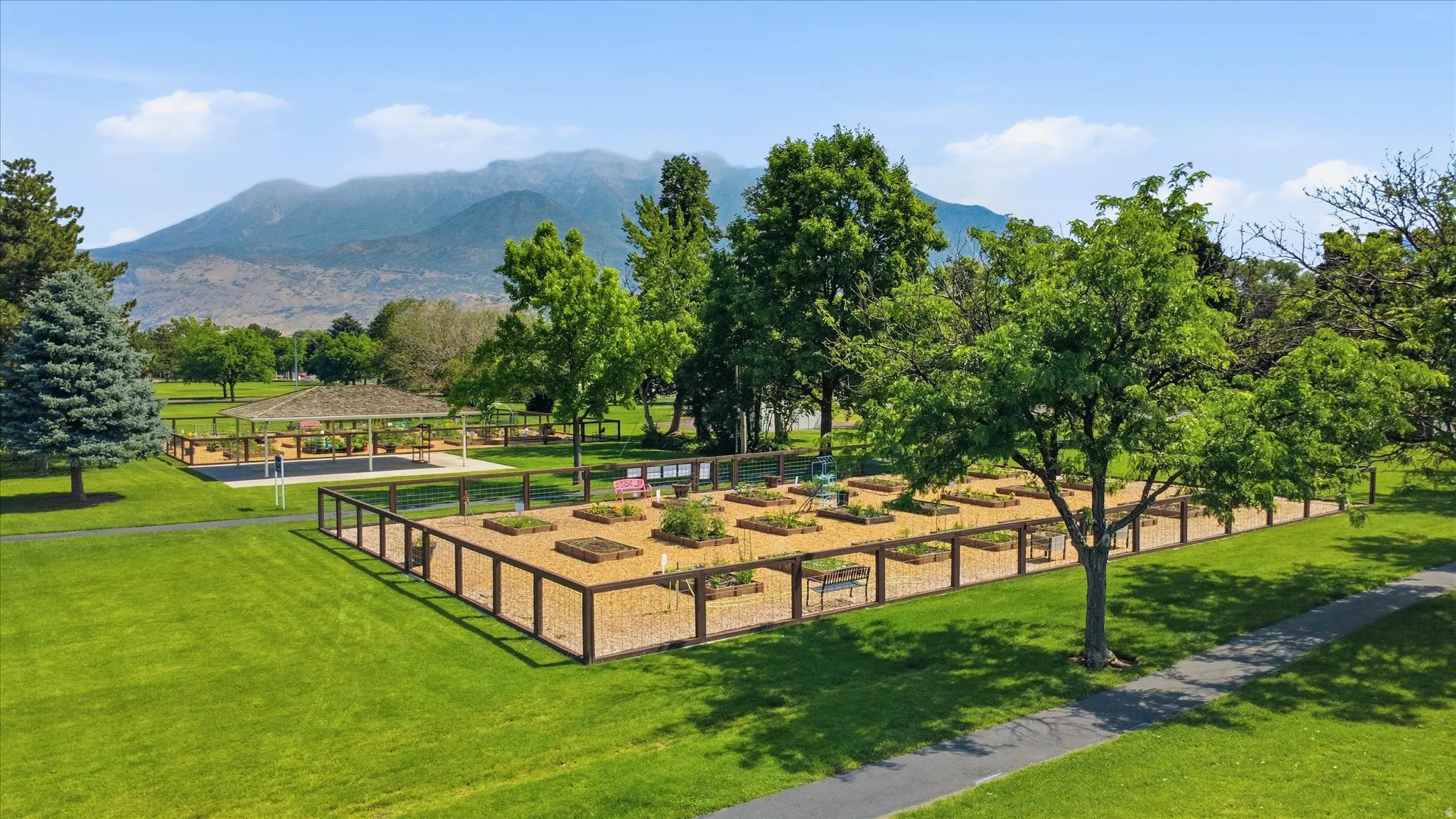 Expansive community garden featuring individual raised beds, perimeter fencing, and a paved pathway
