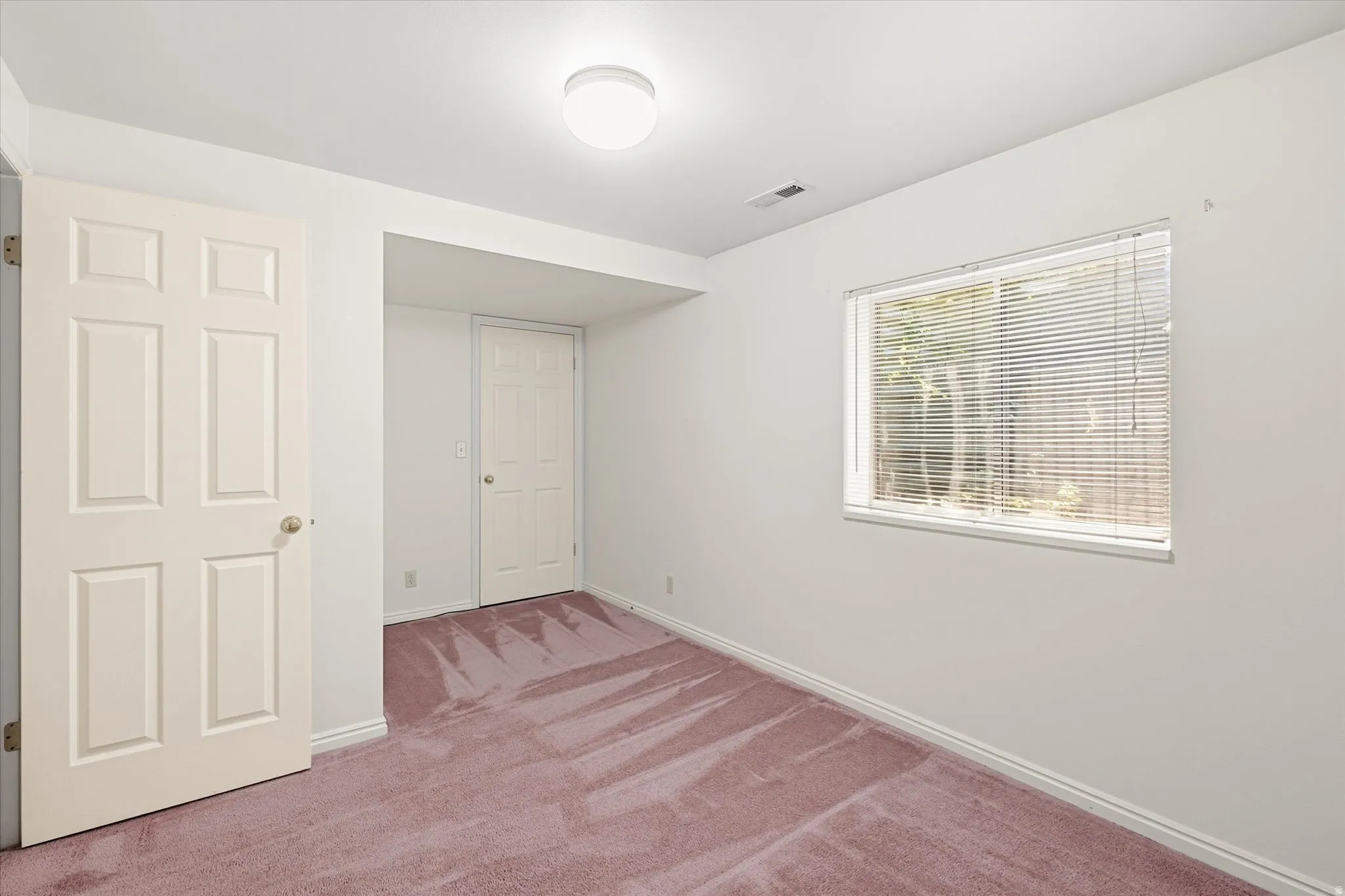 Spacious room featuring carpeting, white walls, and a window with blinds