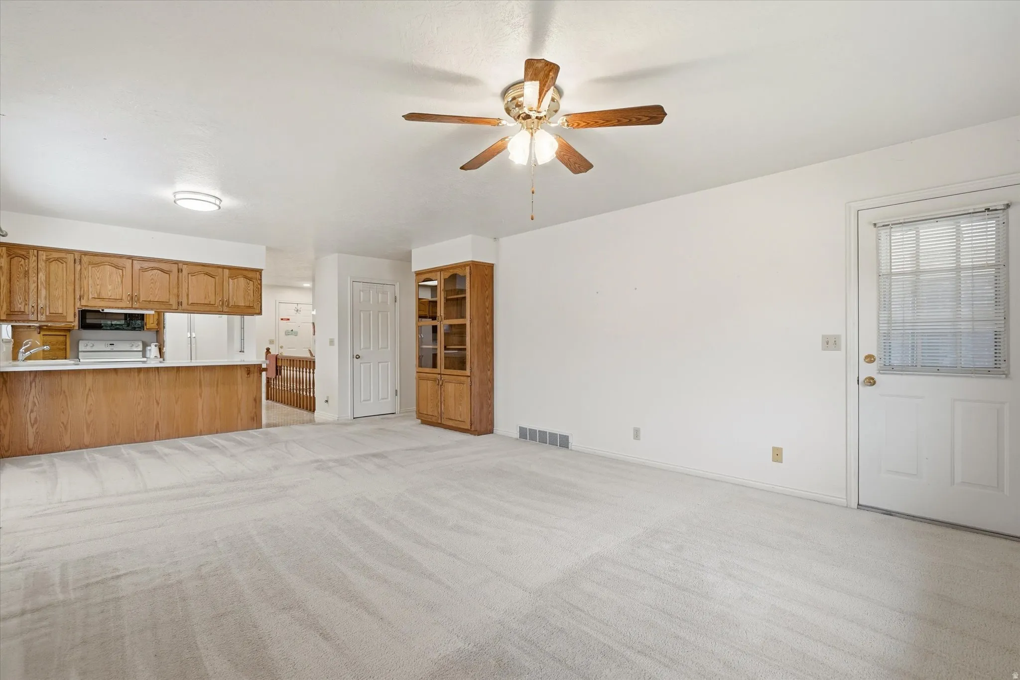 Spacious living area featuring light-toned carpeting and white walls