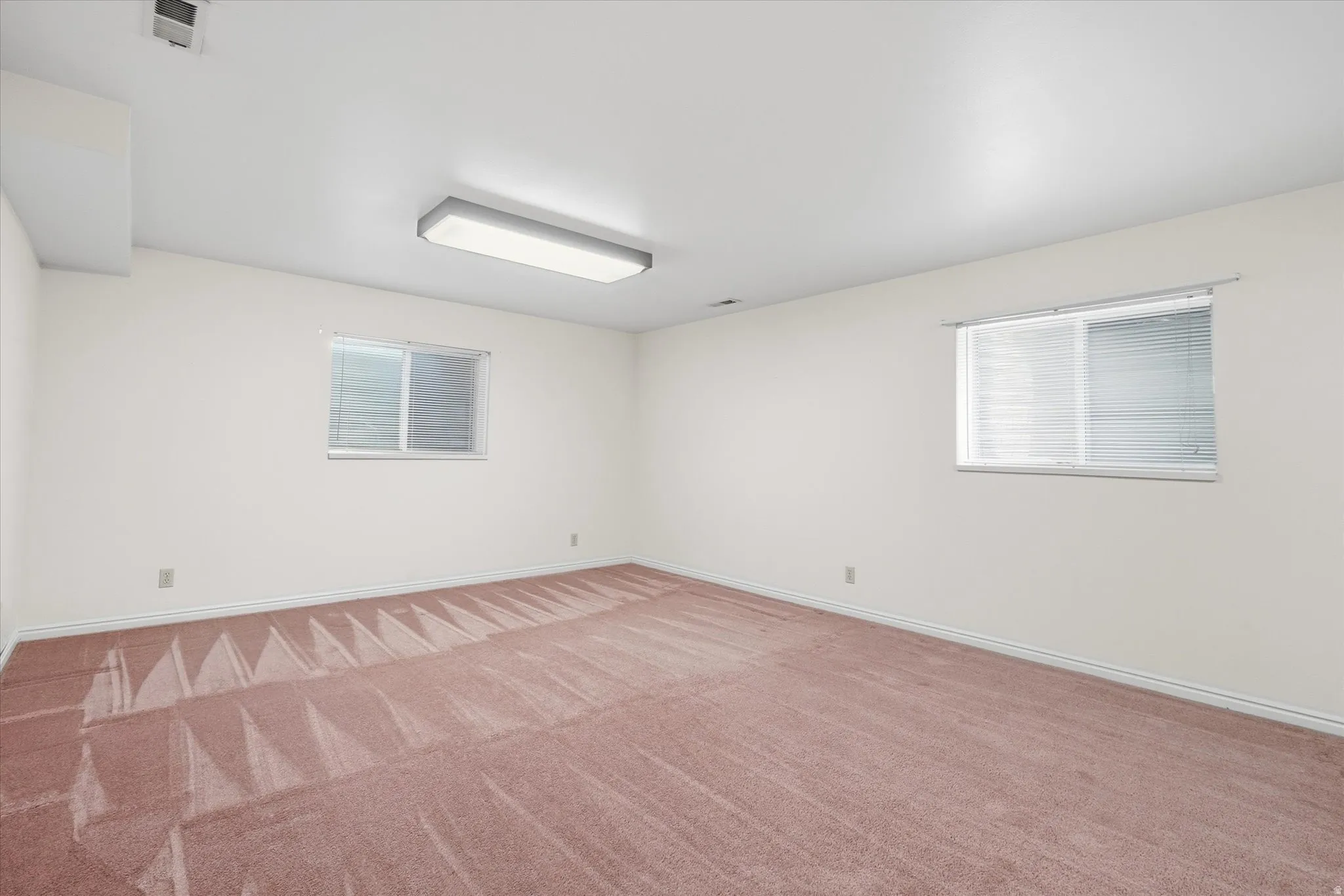 Spacious room featuring neutral white walls and a light pink carpet