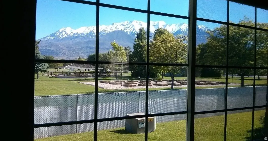 Expansive window offering a mountain backdrop, a fenced perimeter, green lawn, and mature trees