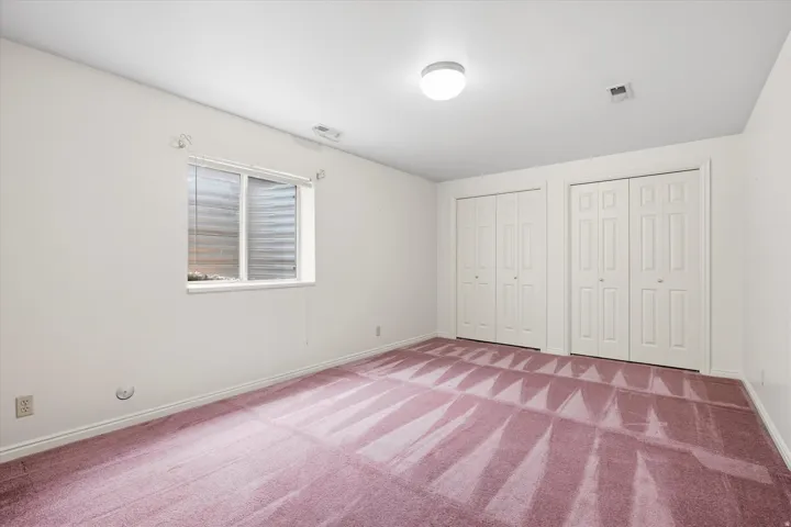 Spacious room featuring two bi-fold door closets, recessed window with blinds, overhead lighting, and carpeted flooring