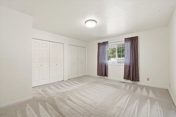 Spacious room featuring light-colored carpeting, multiple bifold closet doors, a window with exterior visibility, and a ceiling-mounted light fixture