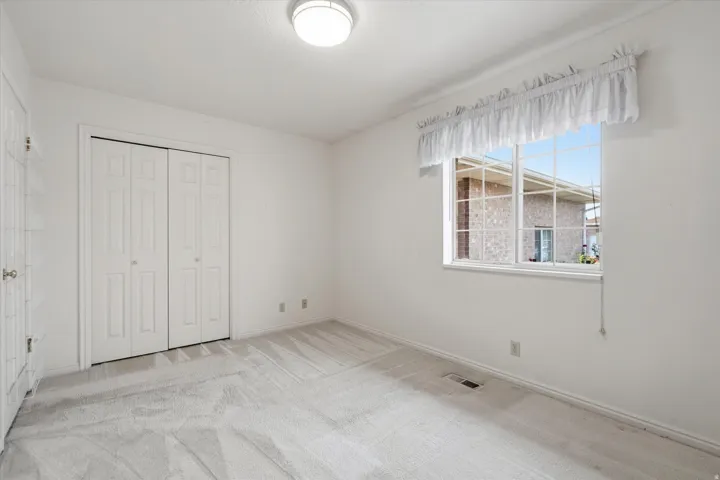 Light-colored carpeting complements white walls in this room, featuring a double bi-fold closet and a large window with horizontal grids