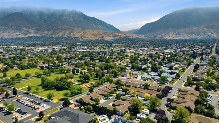 Expansive aerial landscape featuring a residential neighborhood with a large public park, abundant mature trees, mountain backdrop, and clear skies