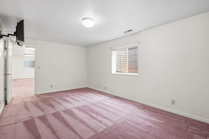 Spacious interior room featuring wall-to-wall carpeting, a flush-mount ceiling light fixture, and a window with blinds