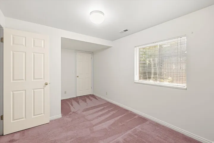 Spacious room featuring carpeting, white walls, and a window with blinds