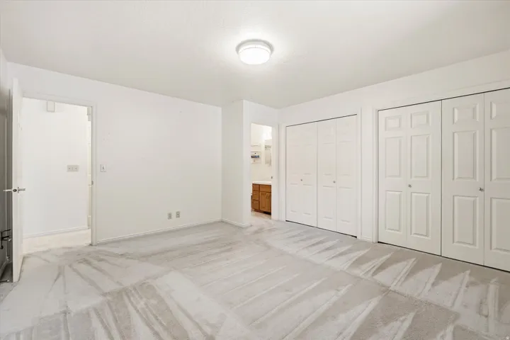 Carpeted room featuring multiple closet doors with bifold and paneled designs, a flush-mount ceiling light fixture, and white painted walls