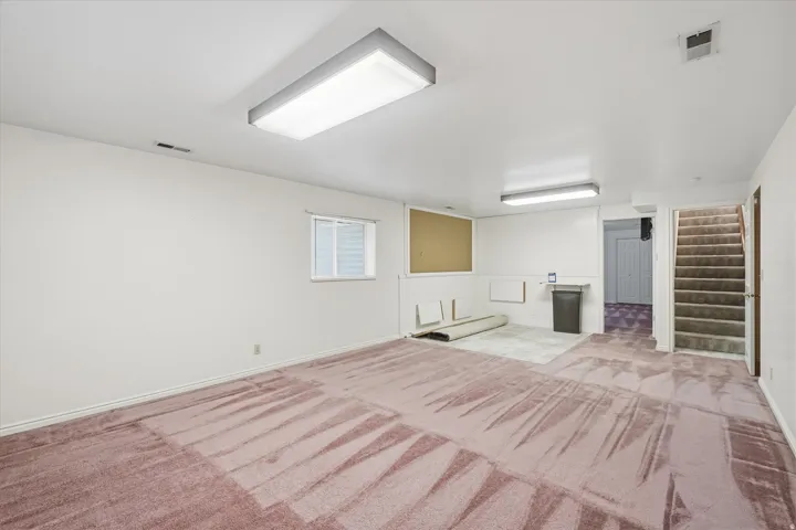 Lower level room with recessed window, fluorescent overhead lighting, and mixed flooring including carpet and tile