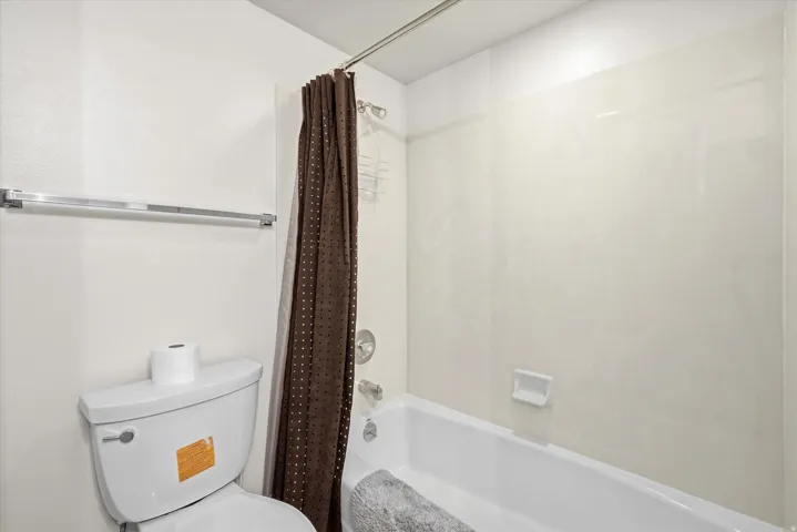 White bathtub with integrated shower, white wall tile surround, and chrome fixtures