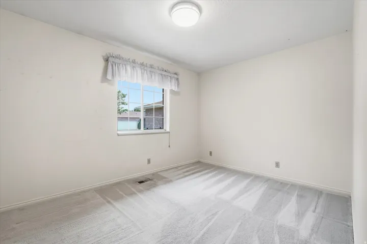 Room featuring light gray carpet, white walls, and a window with a white frame and grilles