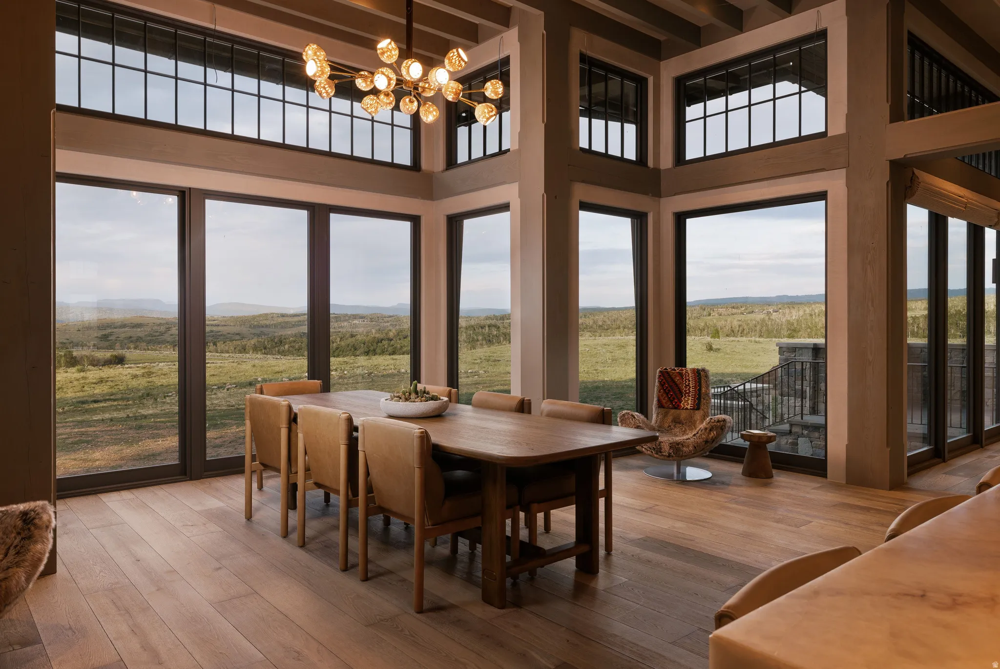 Spacious dining area featuring expansive windows, wood-finish flooring, exposed ceiling beams, and a contemporary chandelier