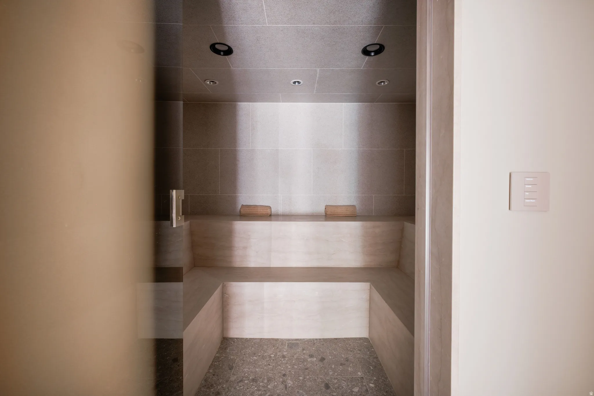 Steam room featuring tiled walls, built-in benches, recessed lighting, and a pebble-finish floor