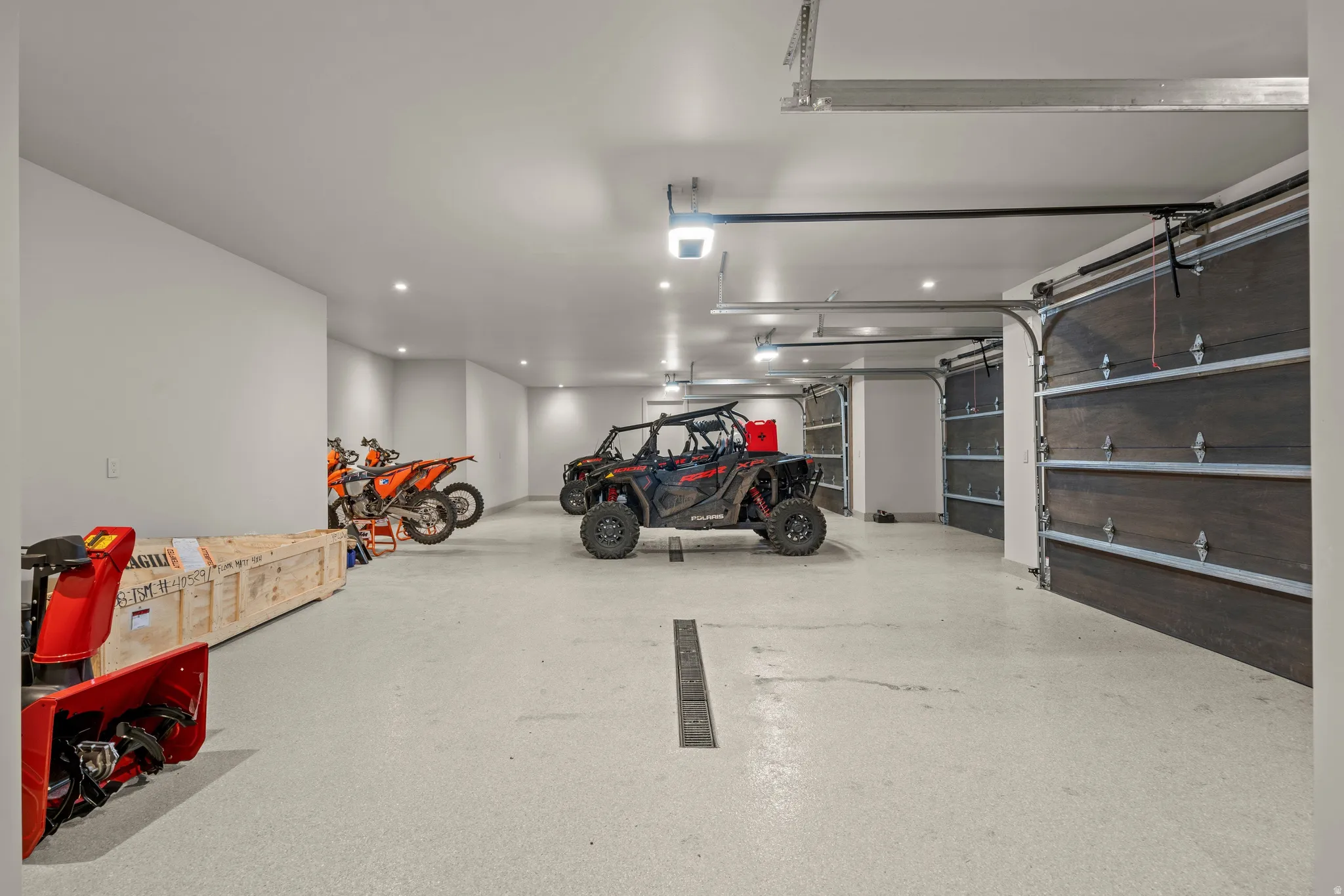 Expansive garage featuring multiple dark wood-panel garage doors, light-colored epoxy flooring, recessed lighting, and bright white walls
