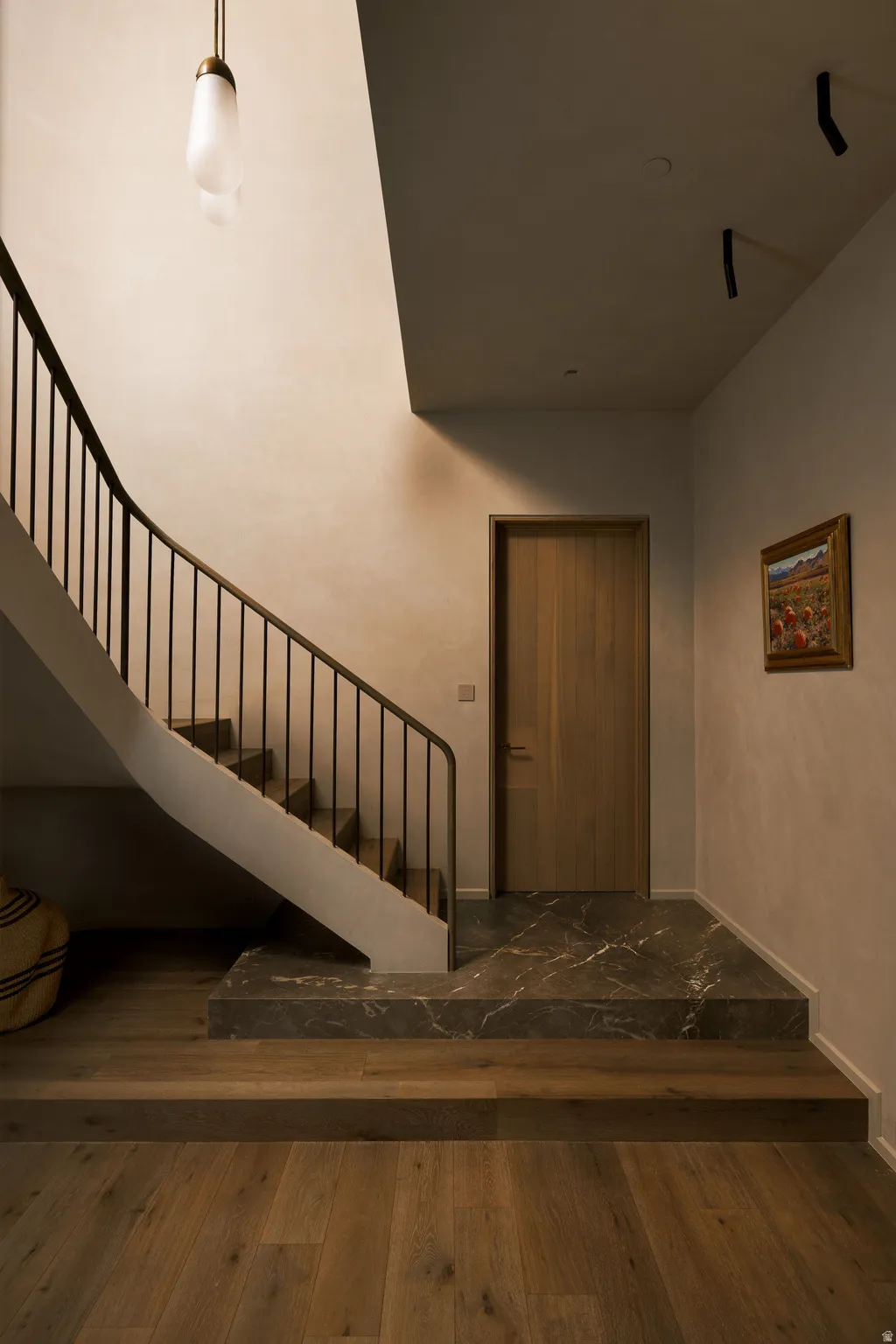 Curved staircase with a dark metal railing, featuring wood-finish flooring and a contrasting stone landing
