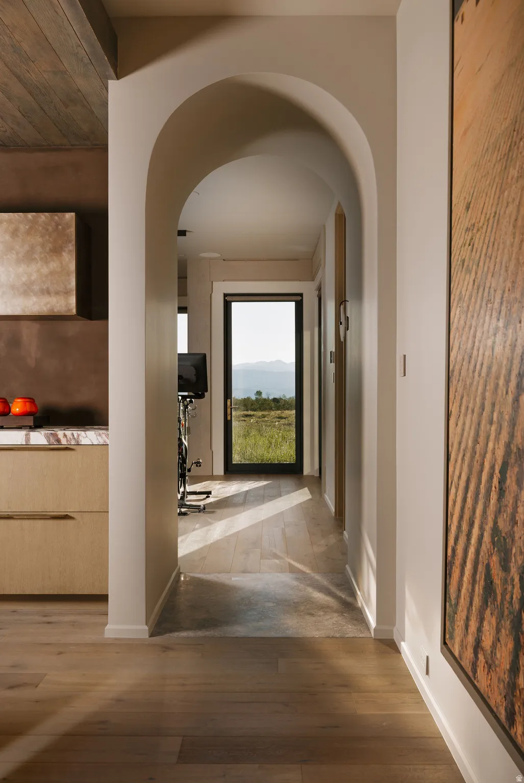 Archway entry to a hallway featuring light wood-finish flooring, recessed lighting, and a full-light exterior door