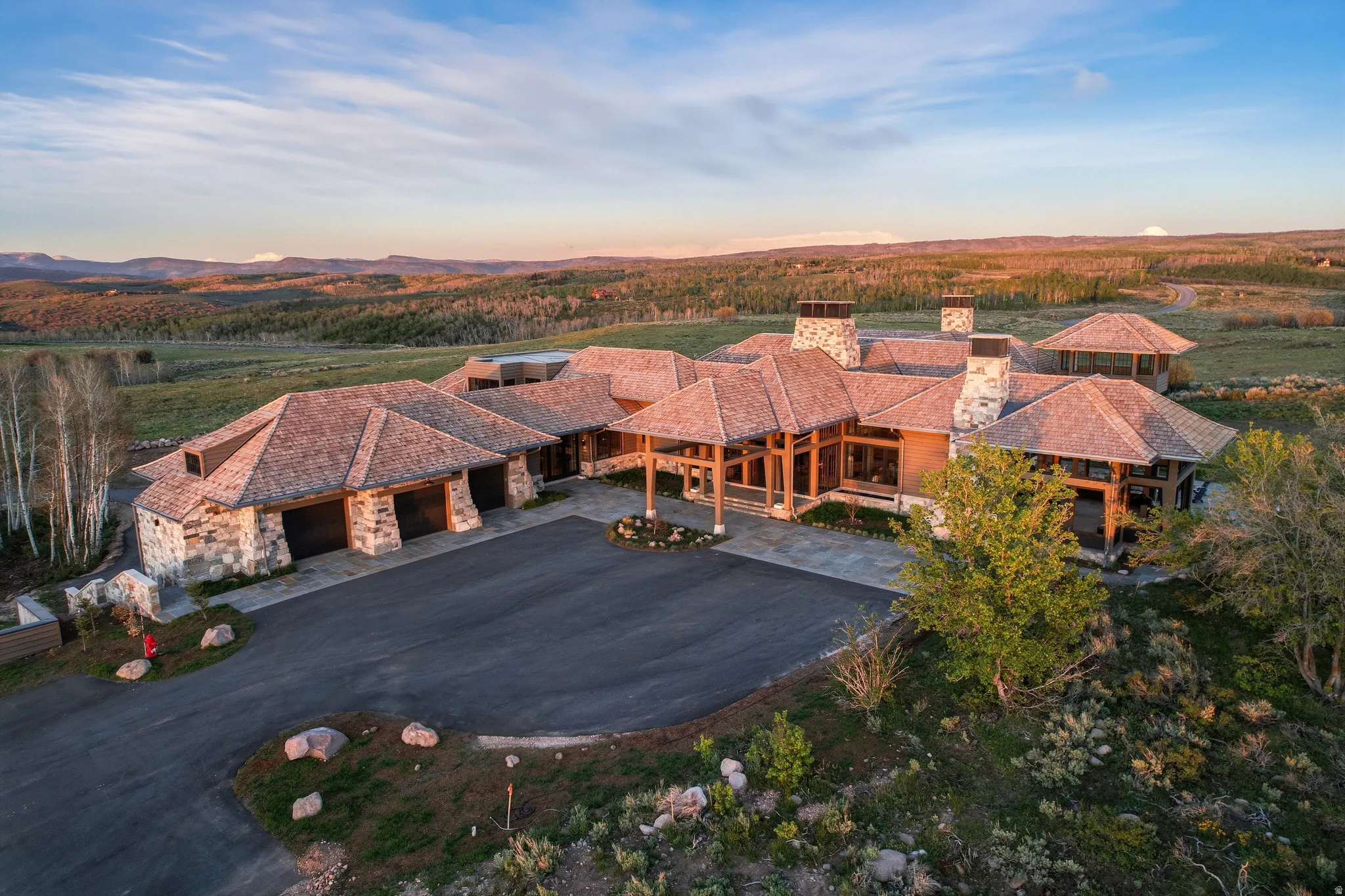 Sprawling estate featuring extensive stone siding, multiple gabled roofs with shake shingles, and a large paved driveway