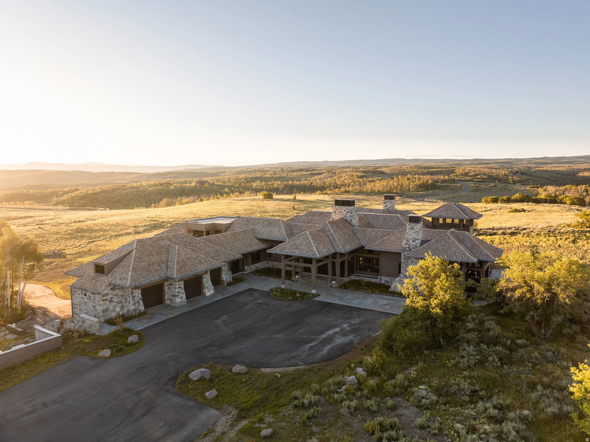 Sprawling stone and timber estate featuring multiple gables, extensive stone chimneys, and a multi-car garage