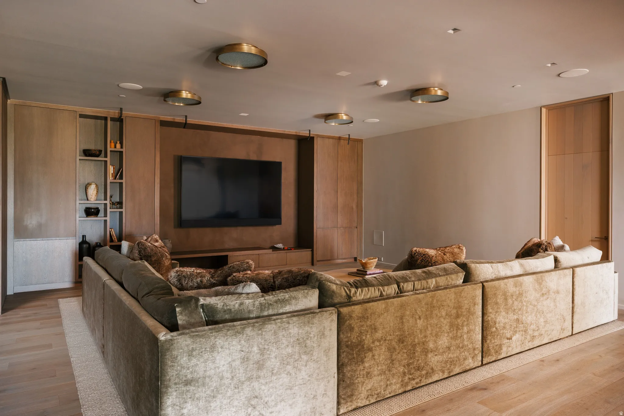 Integrated wall-mounted television with built-in media console, custom cabinetry, recessed ceiling lights, and light wood-finish flooring