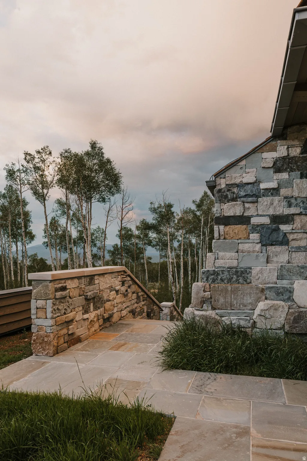 Stone exterior with varied natural hues, featuring a stone retaining wall and a flagstone patio